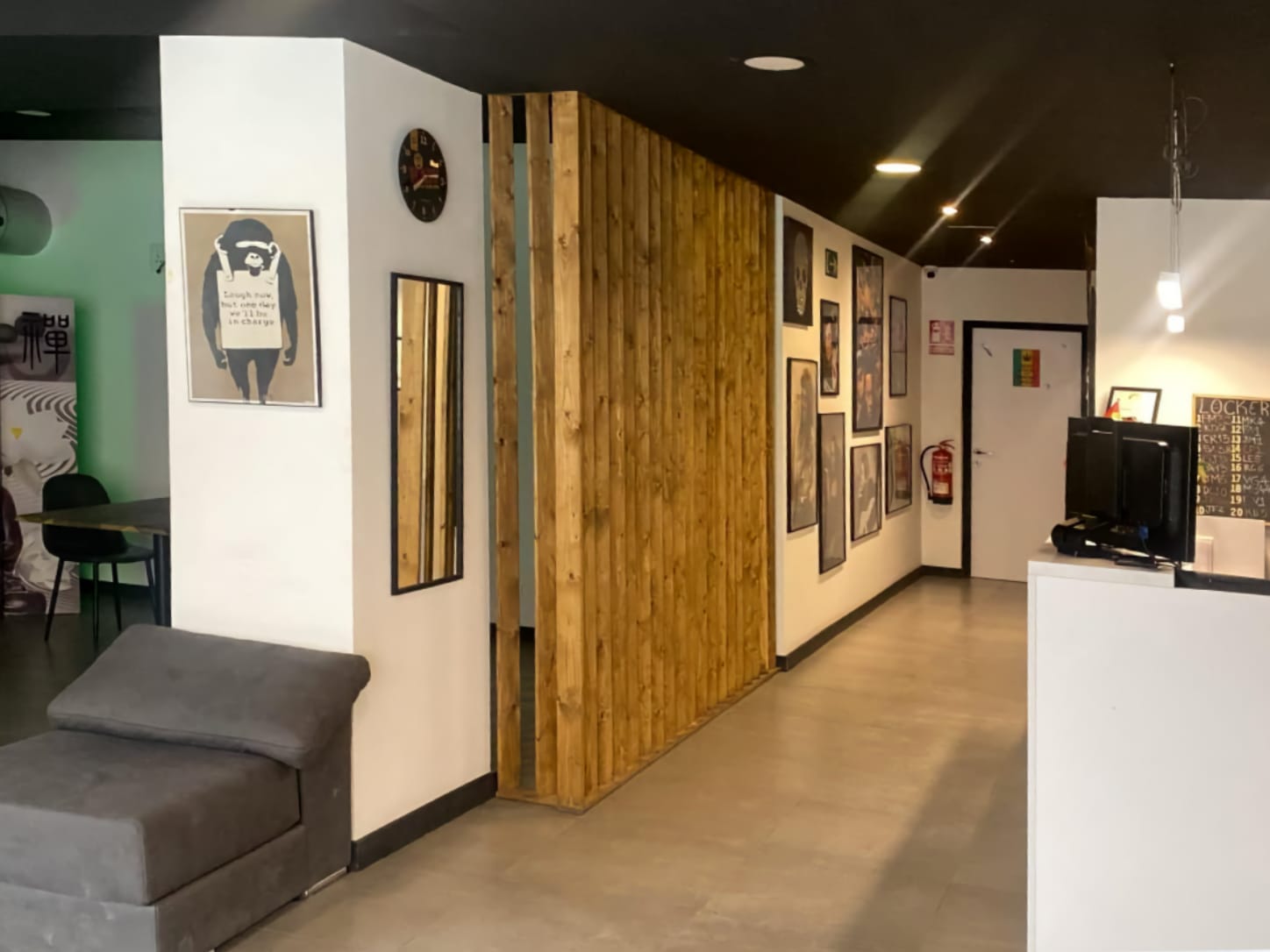 Der Empfangsbereich und das moderne Interieur im Four Twenty Cannabis Club in Valencia, mit einer Holzlamellentrennwand, gerahmter Wandkunst und einem grauen Sessel.