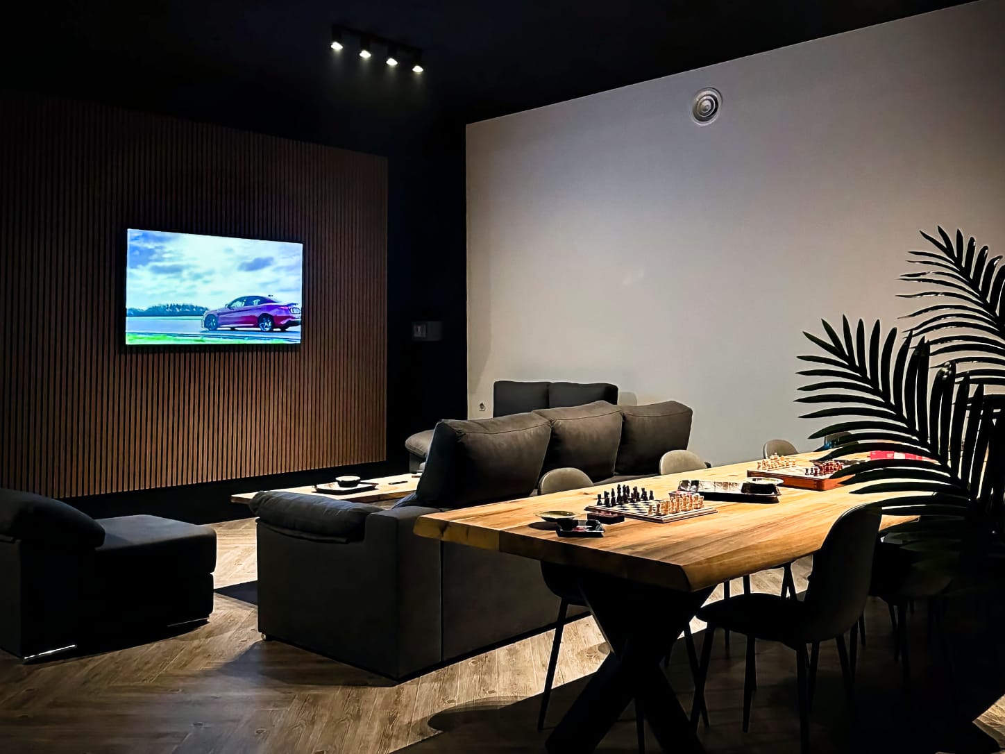 Der gem&uuml;tliche Lounge-Bereich im Four Twenty Cannabis Club in Valencia, mit dunklen Sofas vor einem gro&szlig;en Fernseher an einer Holzlamellenwand und Schachspielen auf einem langen Holztisch.