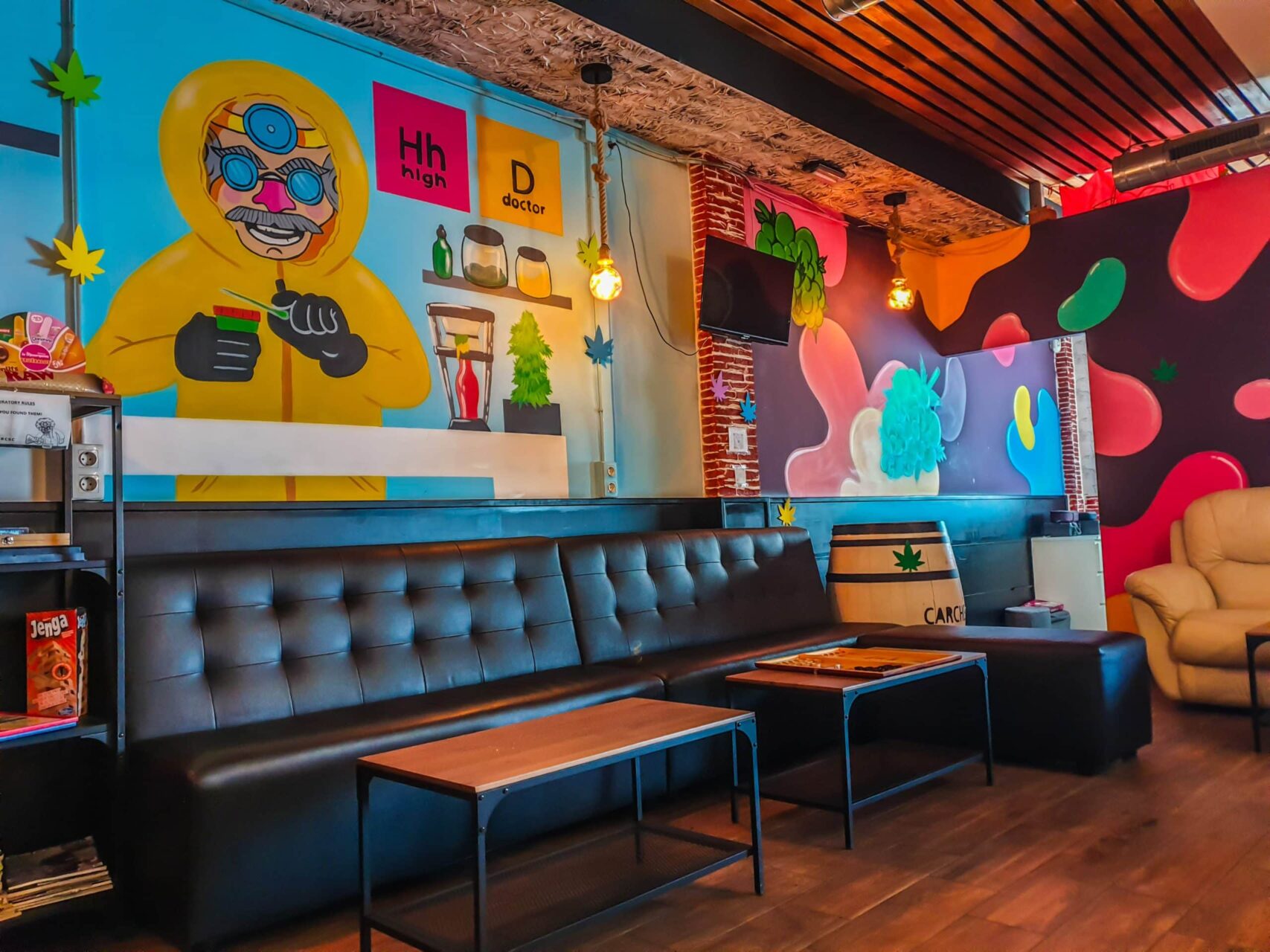 Innenraum des High Doctor Social Clubs in Alicante mit bunten Graffiti-W&auml;nden, schwarzen Ledersofas und Holzb&ouml;den.