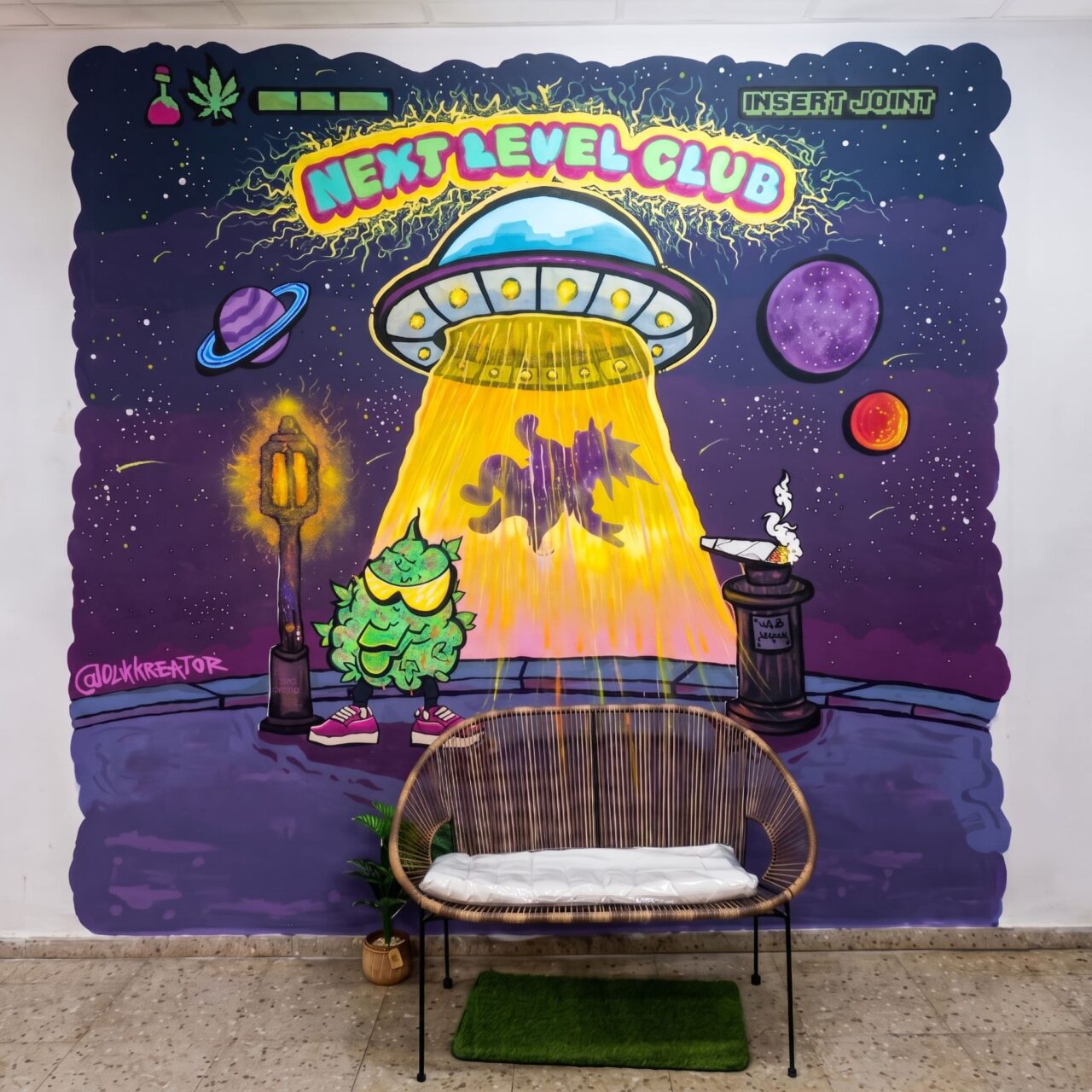 Innenraum des Cannabis-Clubs Next Level Club in Valencia: eine geflochtene Bank vor einem UFO-Graffiti.
