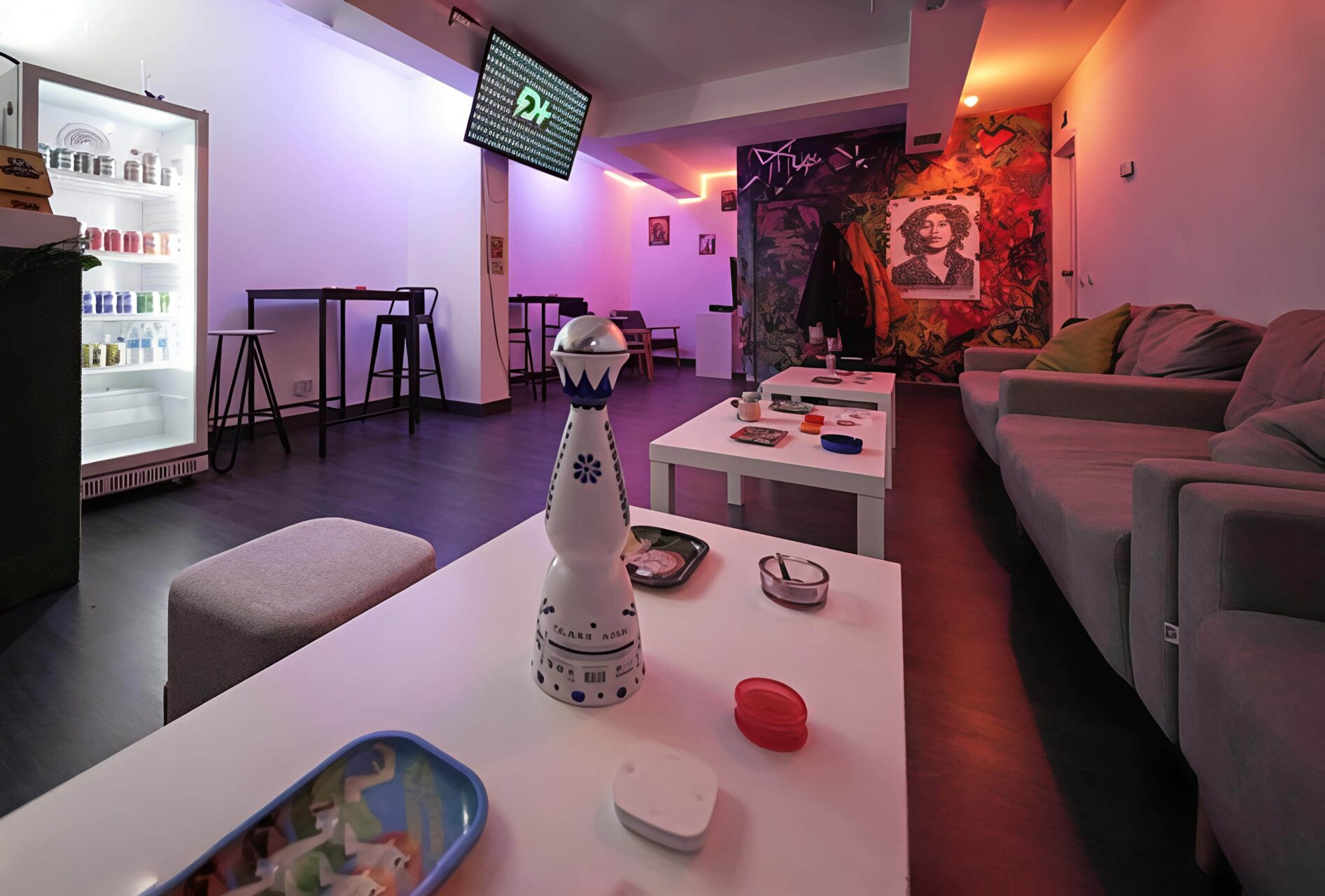Lounge-Bereich im Valhalla Cannabis Club in Madrid mit blauer und oranger Neonbeleuchtung, niedrigen Couchtischen und Graffiti-Wandkunst.