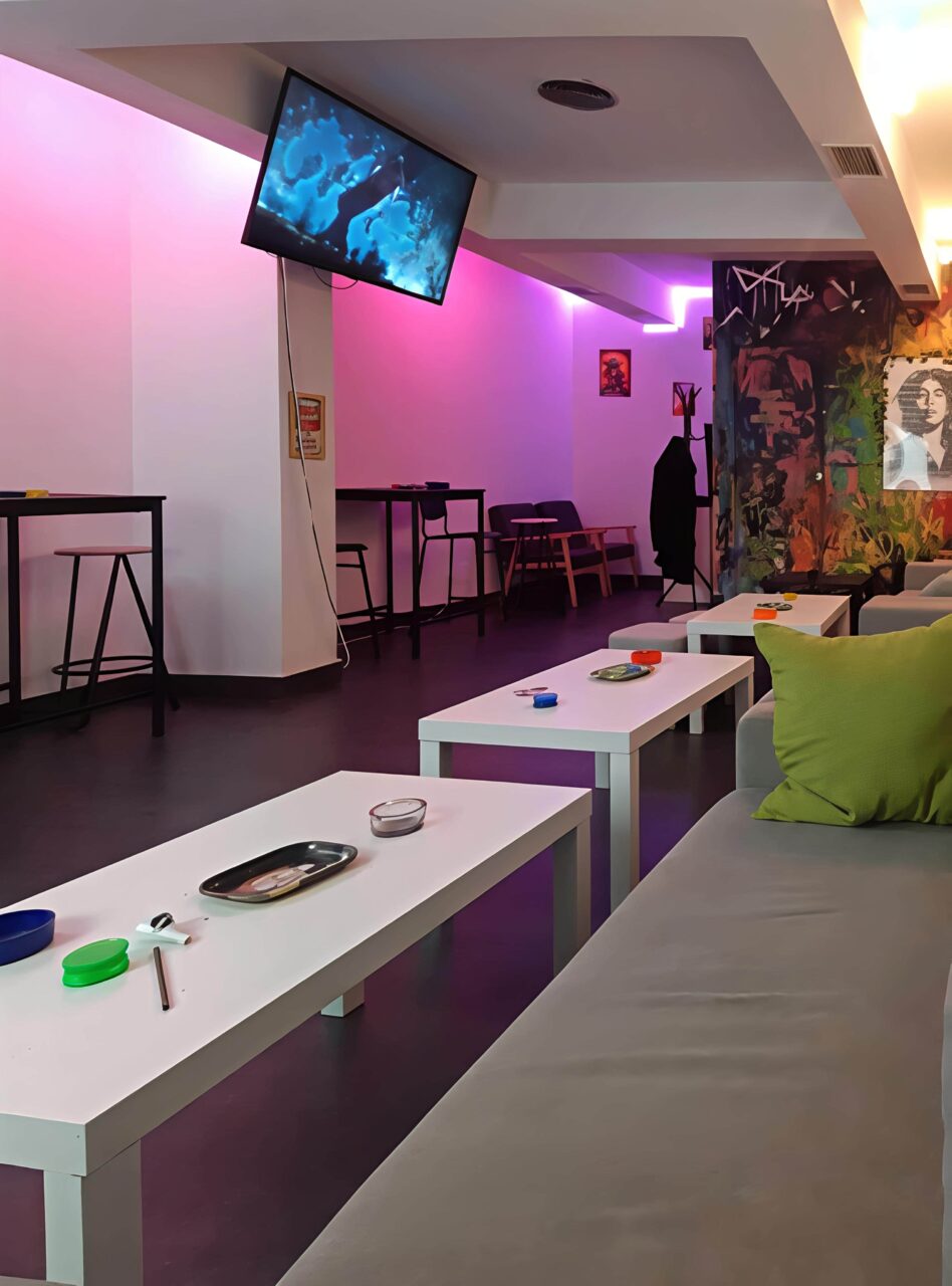 Modernes Lounge-Interieur mit violetter Neonbeleuchtung im Valhalla Cannabis Club in Madrid, mit niedrigen Couchtischen, Sofas und Barhockern.